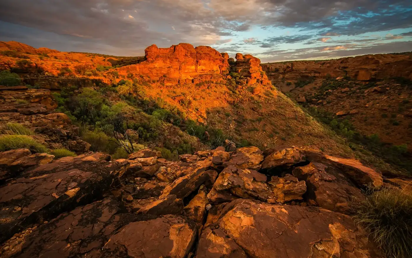 A red sandstone canyon lit low by the sun, under broken cloud